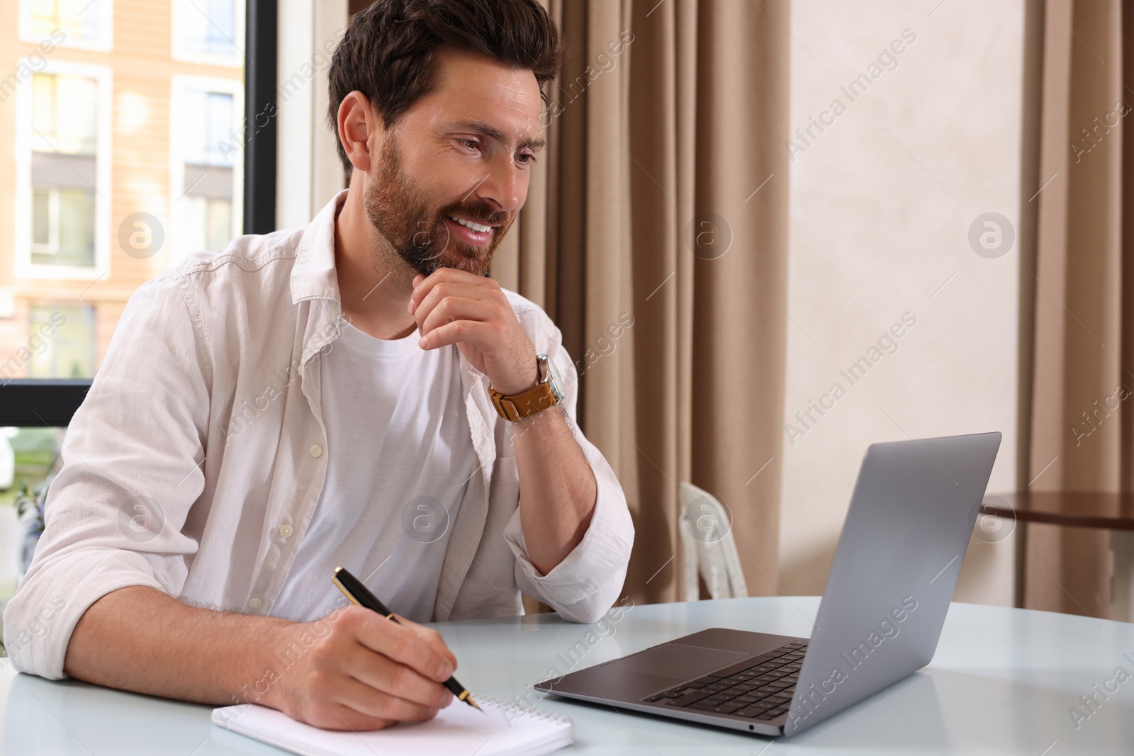 Photo of Man working on laptop and writing something at table in cafe