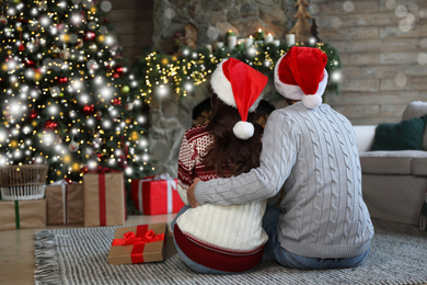 Image of Young couple wearing Santa hats in living room decorated for Christmas