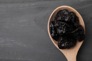 Sweet dried prunes in spoon on grey wooden table, top view. Space for text