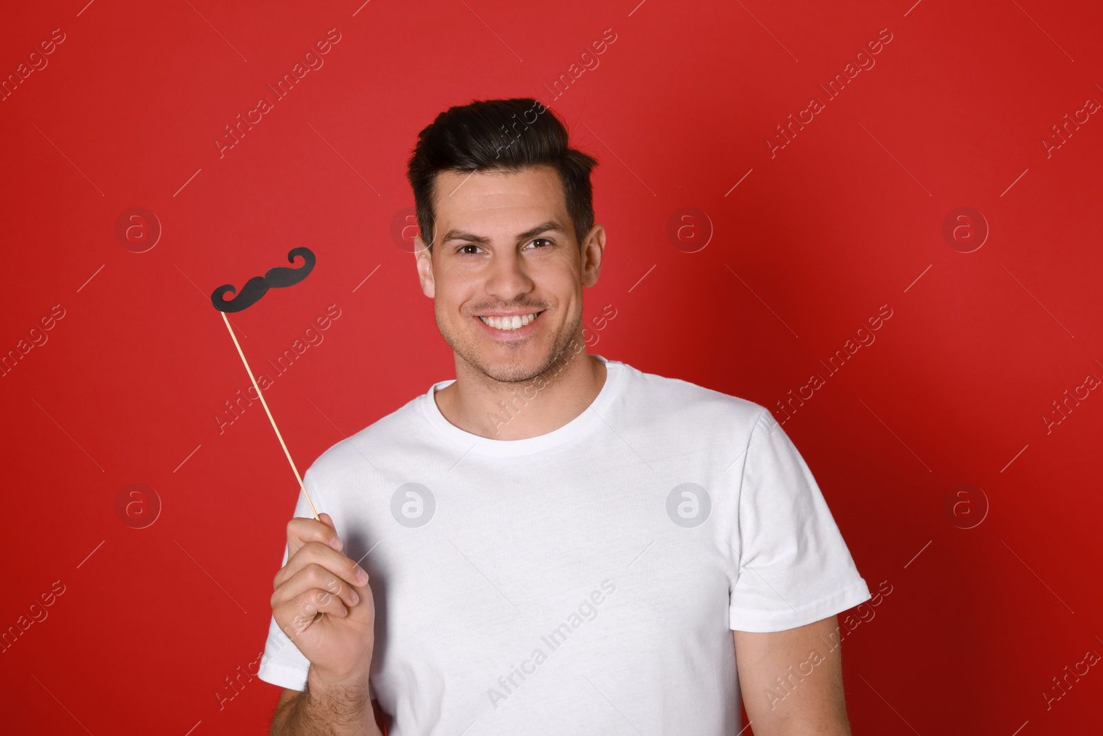 Photo of Happy man with fake mustache on red background