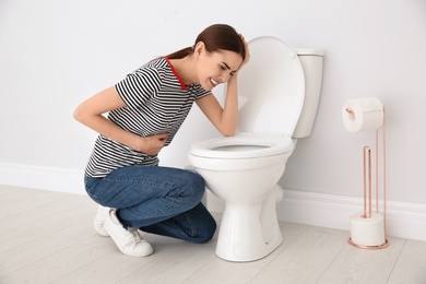 Photo of Young woman suffering from nausea over toilet bowl indoors