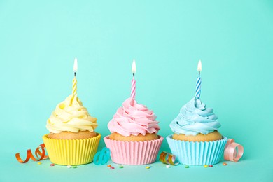 Photo of Delicious birthday cupcakes with burning candles, sprinkles and streamers on turquoise background