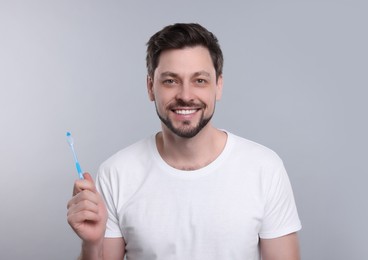 Photo of Happy man holding toothbrush on light grey background