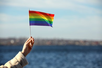 Photo of Woman holding bright LGBT flag near river, closeup. Space for text
