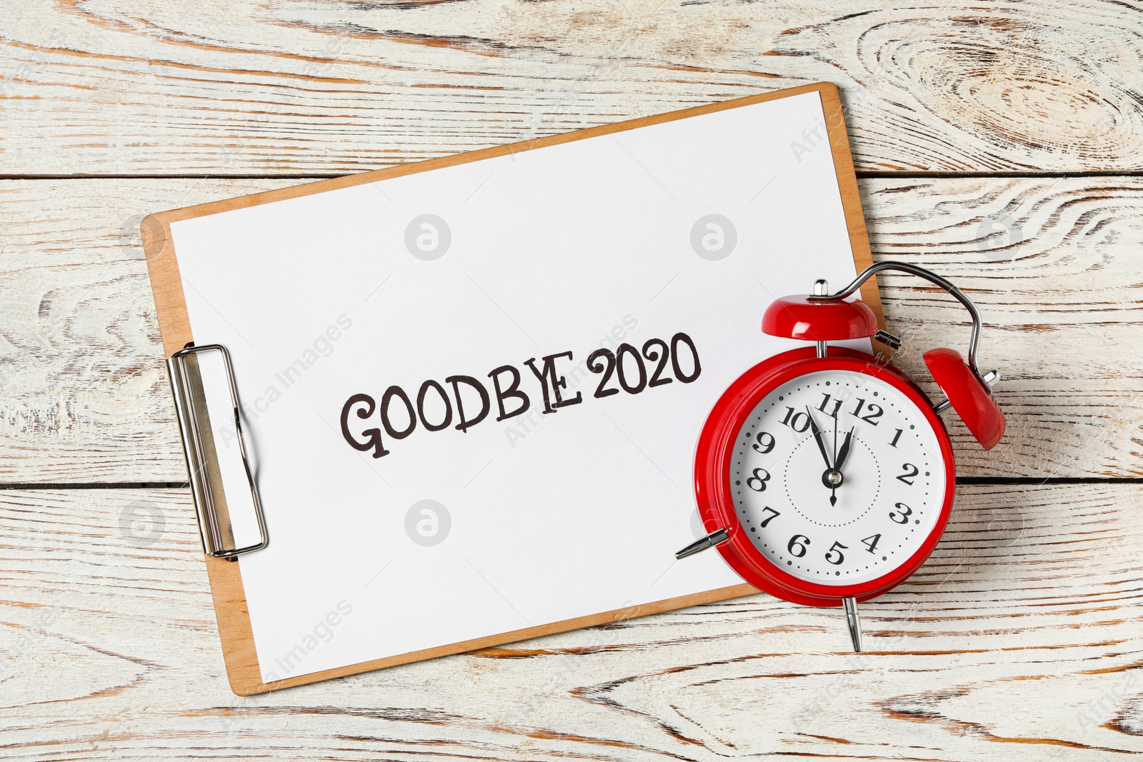 Photo of Clipboard with phrase Goodbye 2020 and alarm clock on white wooden table, flat lay