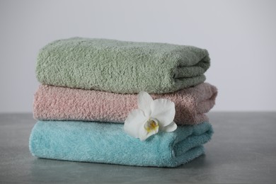 Photo of Stacked soft colorful towels with flower on grey table