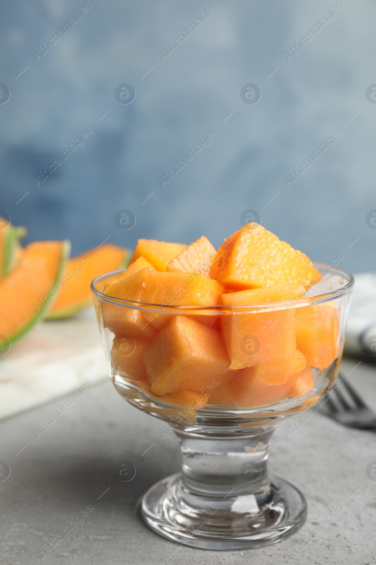 Photo of Cubes of tasty ripe cantaloupe melon in glass bowl on grey table