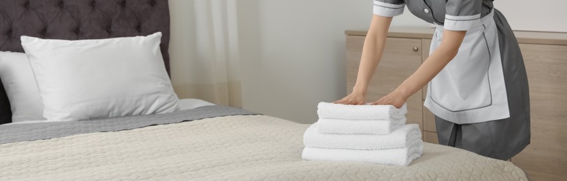Chambermaid putting fresh towels on bed in hotel room, closeup view with space for text. Banner design