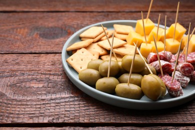 Photo of Toothpick appetizers. Olives, pieces of sausage and cheese on wooden table, space for text