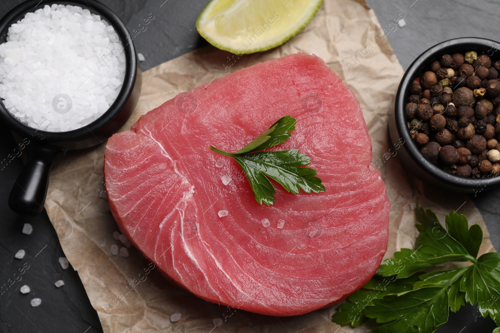 Photo of Raw tuna fillet, parsley and spices on black table, flat lay