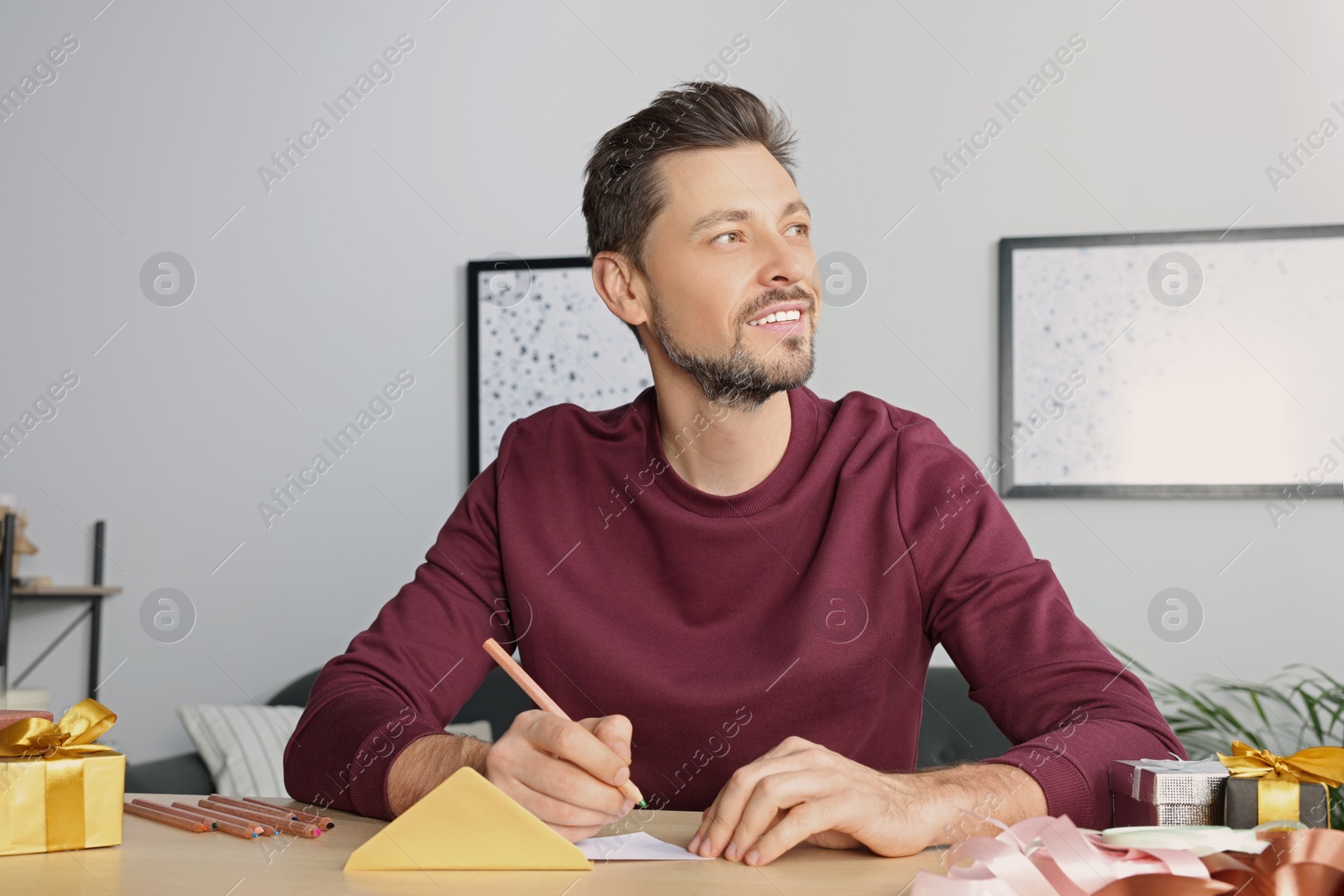 Photo of Man writing message in greeting card at wooden table in room