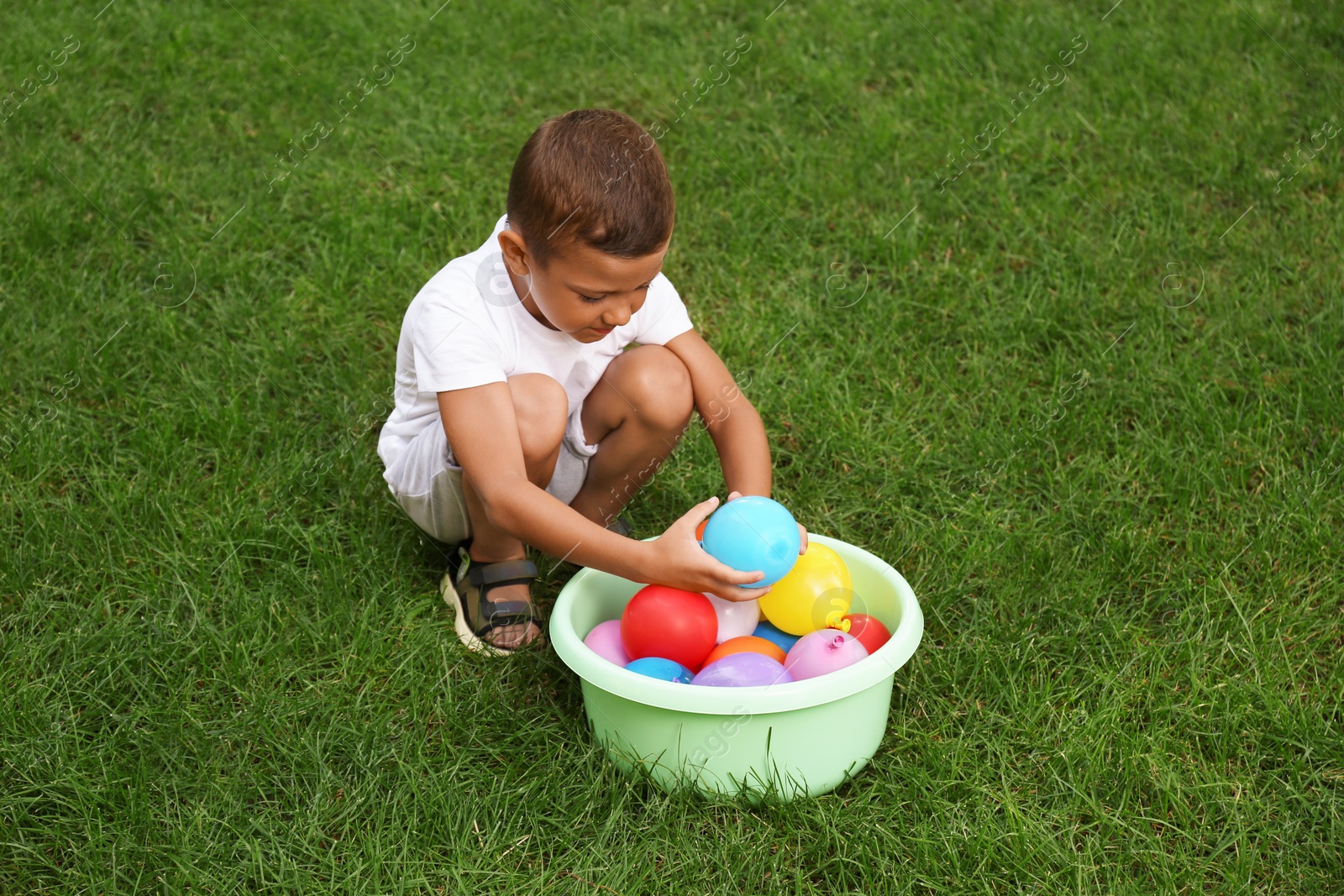 Photo of Little boy with basin of water bombs on green grass