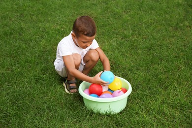 Photo of Little boy with basin of water bombs on green grass