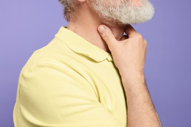 Photo of Senior man suffering from sore throat on light purple background, closeup. Cold symptoms