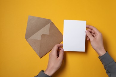 Woman with blank card at orange table, top view. Space for text