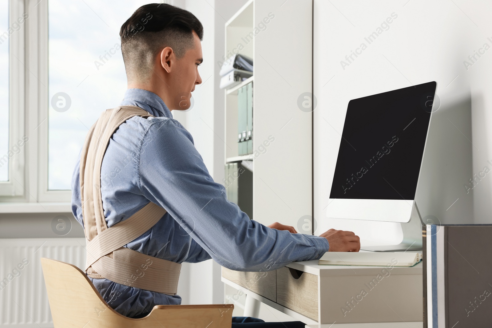 Photo of Man with orthopedic corset working on computer in room