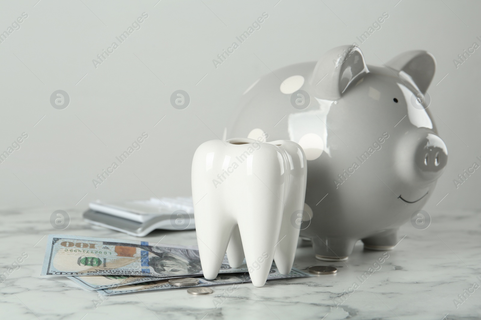 Photo of Ceramic model of tooth, piggy bank and money on white marble table. Expensive treatment