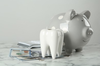 Photo of Ceramic model of tooth, piggy bank and money on white marble table. Expensive treatment
