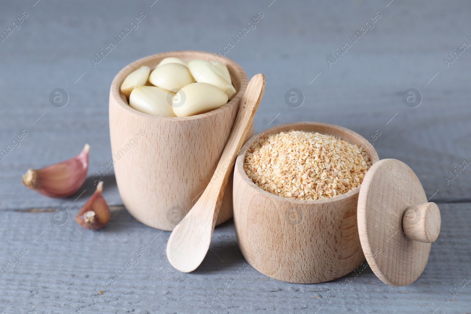 Photo of Dehydrated garlic granules, fresh cloves and spoon on grey wooden table