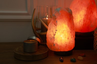 Photo of Himalayan salt lamps, candle and gemstones on wooden table near white wall indoors