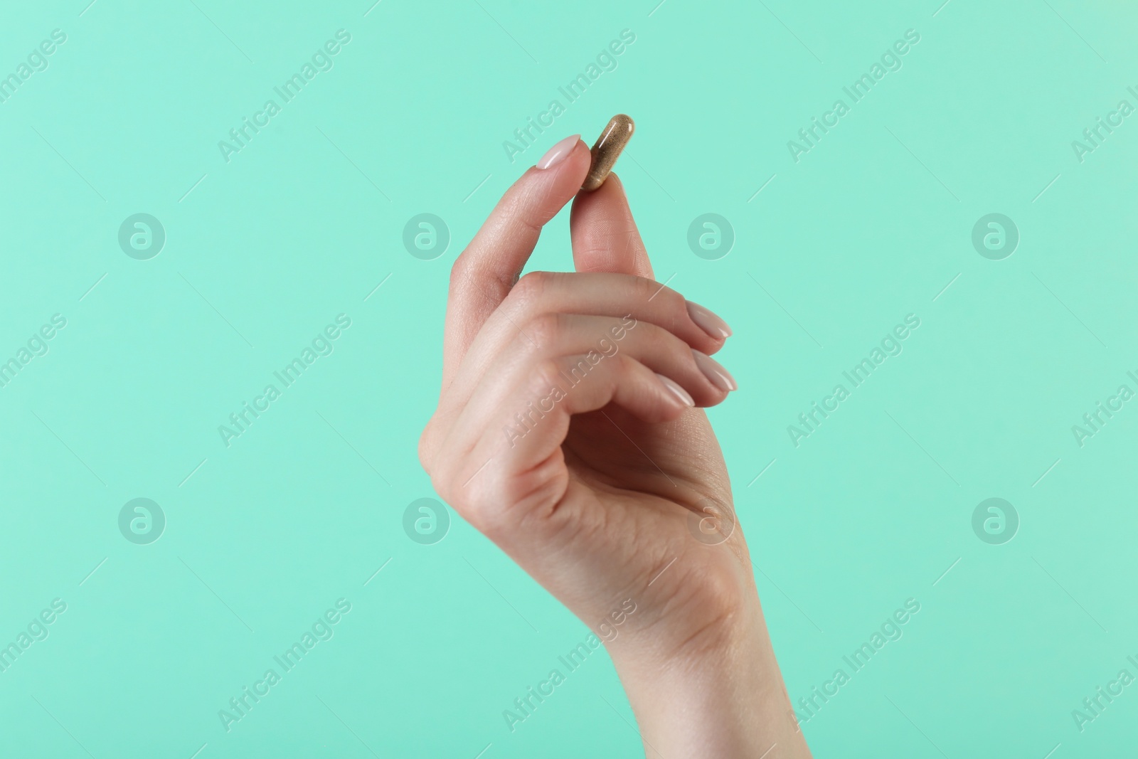 Photo of Woman holding vitamin capsule on turquoise background, closeup. Health supplement