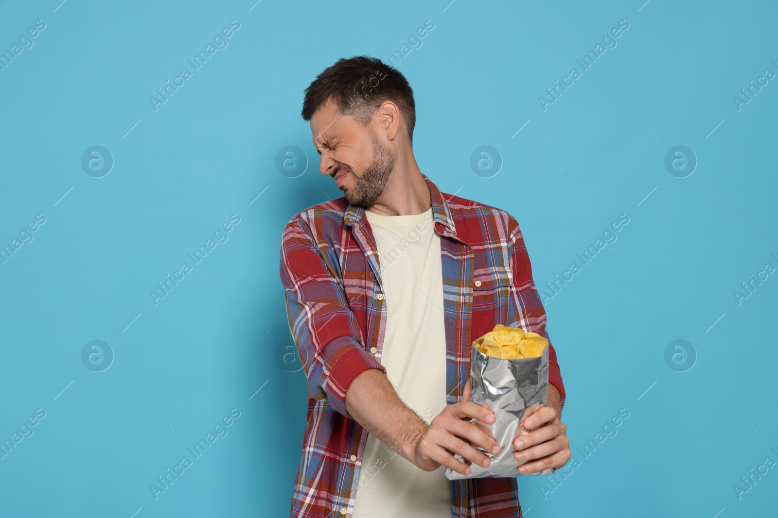 Photo of Handsome man refusing to eat potato chips on light blue background