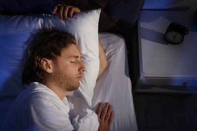 Photo of Handsome young man sleeping on pillow at night, view from above. Bedtime