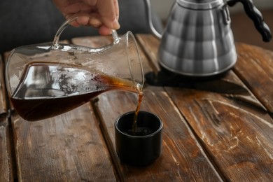 Photo of Barista pouring coffee into cup at wooden table in cafe, closeup