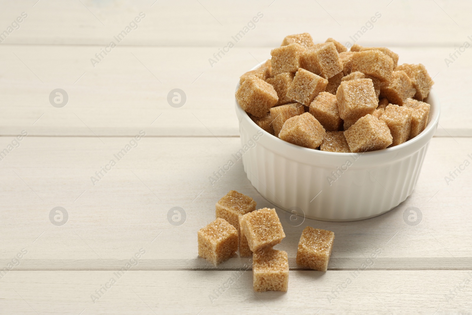 Photo of Brown sugar cubes on white wooden table, space for text