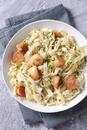 Photo of Delicious scallop pasta with spices in bowl on gray textured table, top view