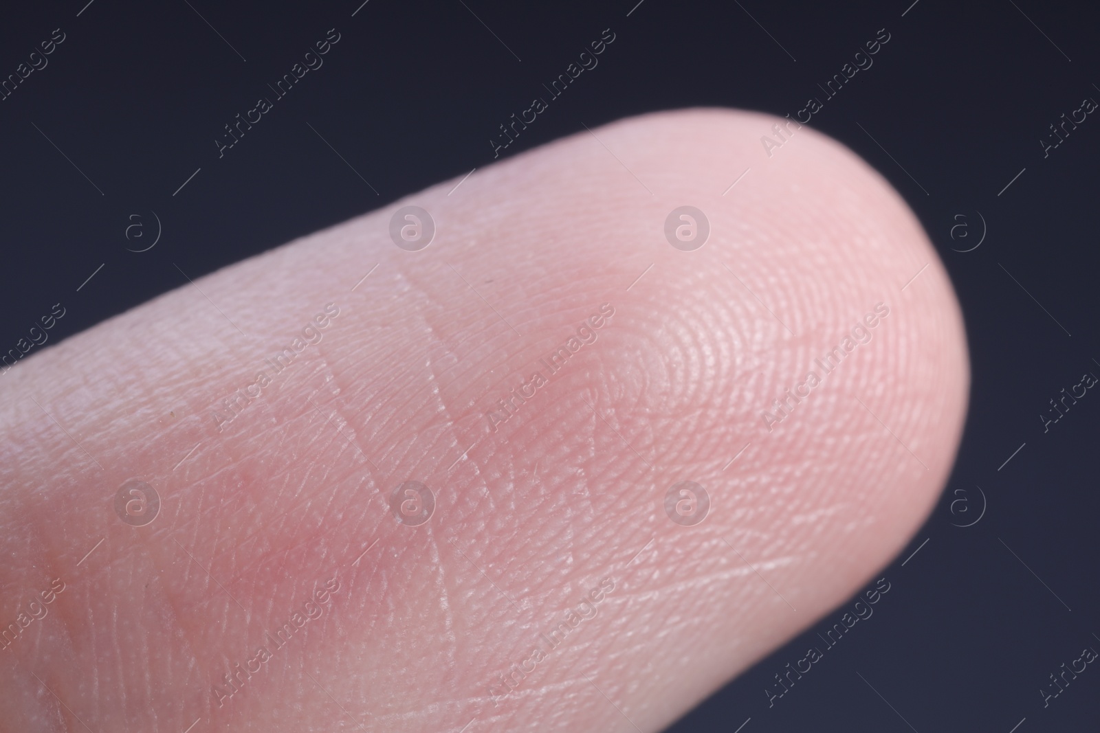 Photo of Finger with friction ridges on dark background, macro view