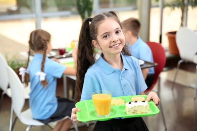 Photo of Cute girl holding tray with healthy food in school canteen