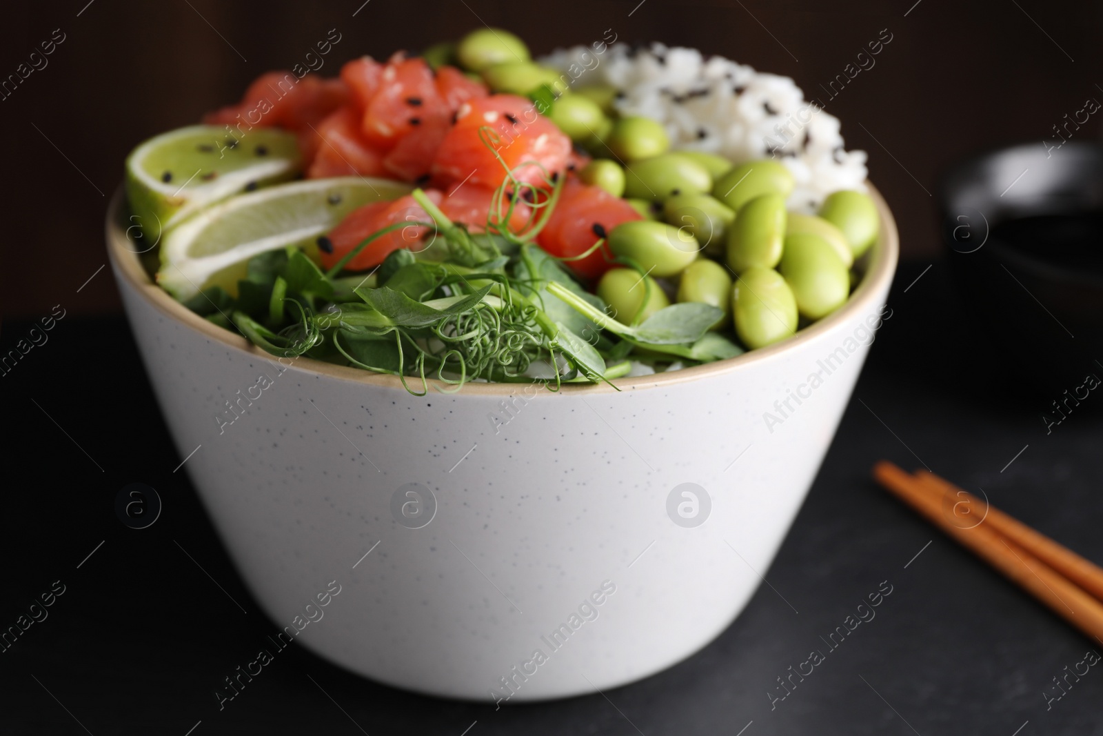 Photo of Delicious poke bowl with lime, fish and edamame beans on black table, closeup