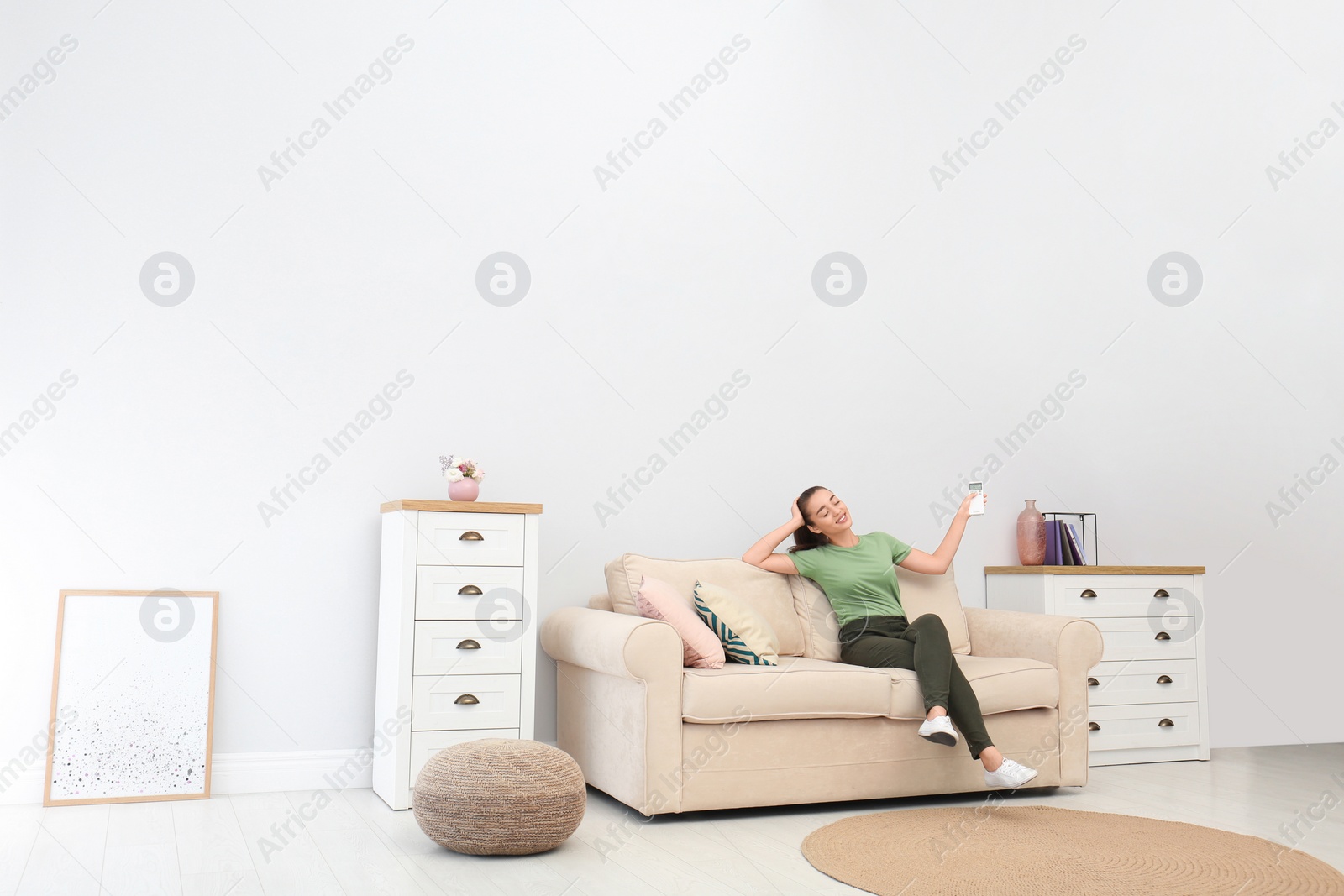 Photo of Happy young woman switching on air conditioner with remote control at home