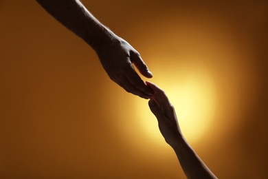 Man reaching for woman's hand on color background, closeup. Help and support concept