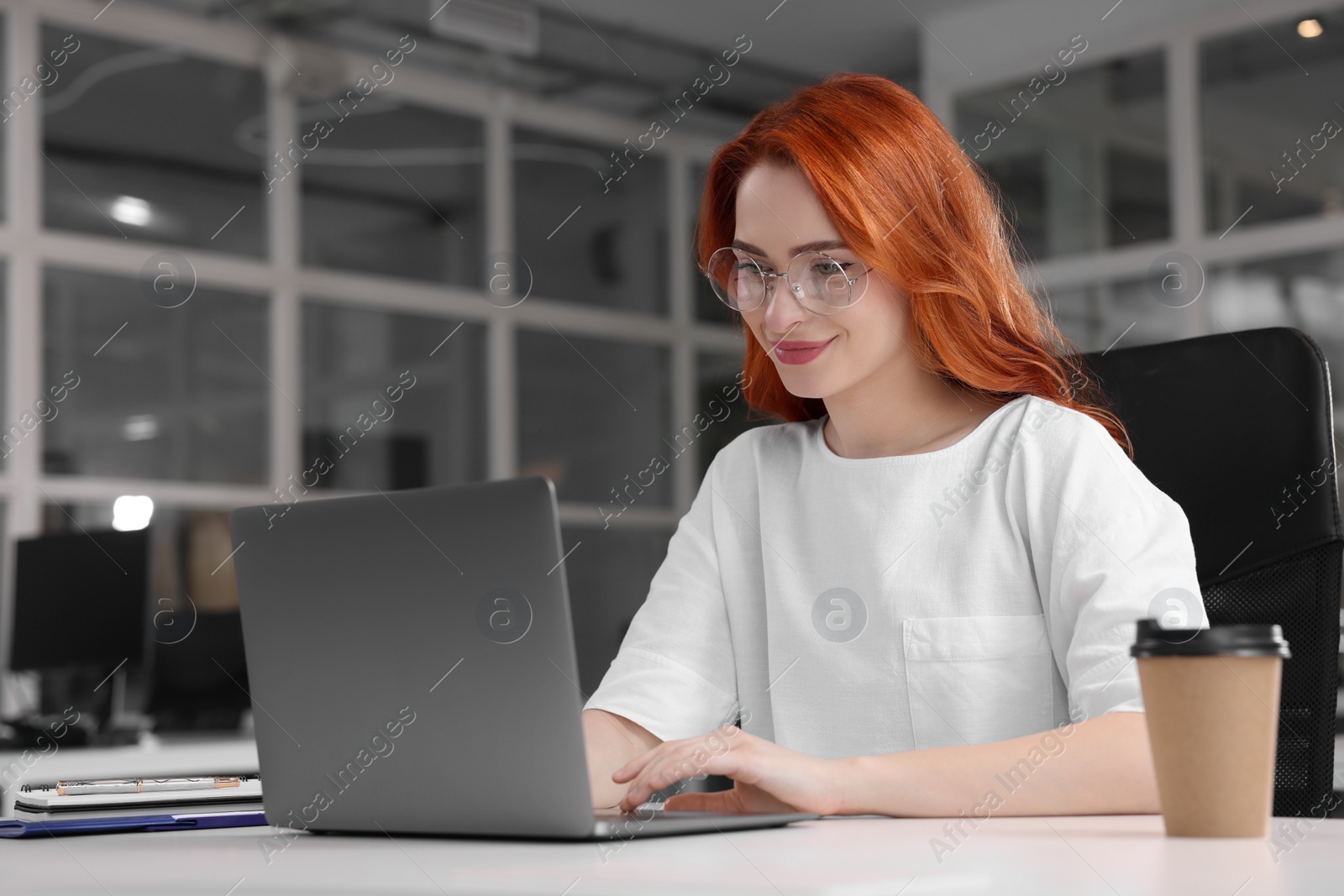 Photo of Happy woman working with laptop at white desk in office