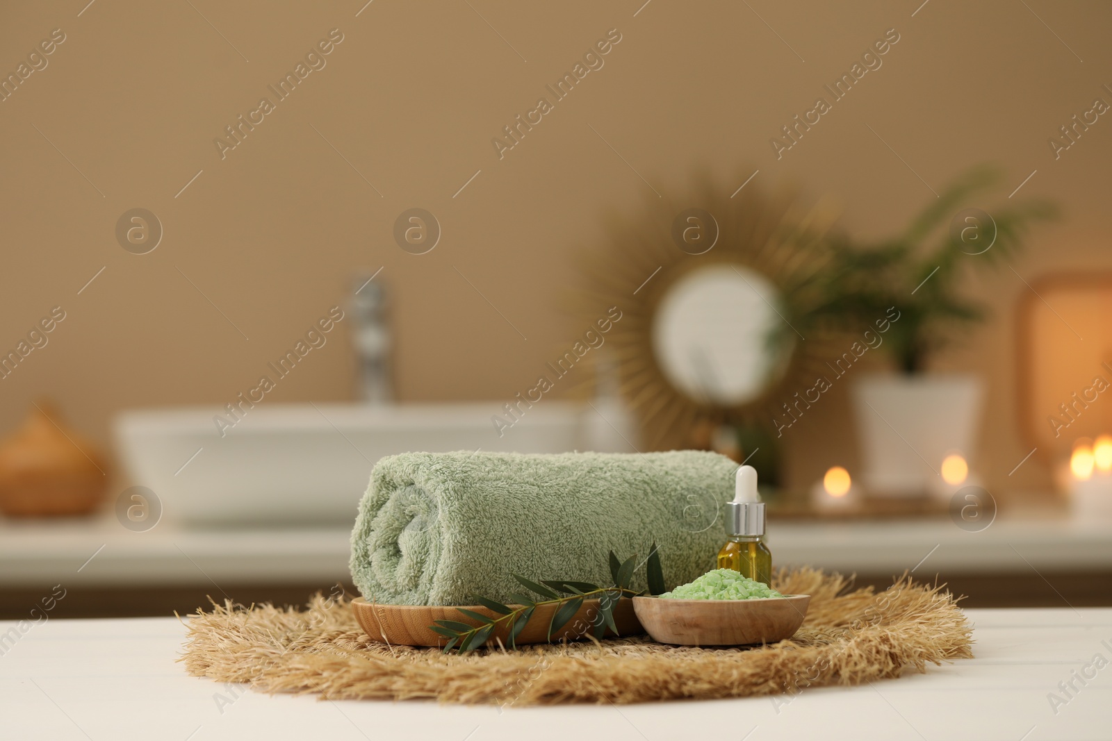 Photo of Spa composition. Rolled towel, cosmetic product, sea salt and twig on table indoors. Space for text