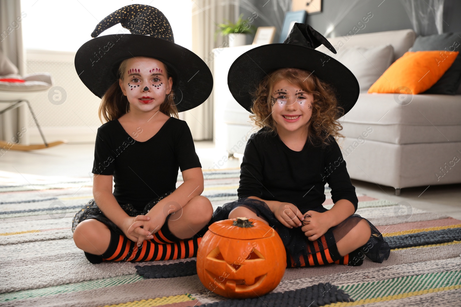 Photo of Cute little girls with pumpkin head jack lantern wearing Halloween costumes at home