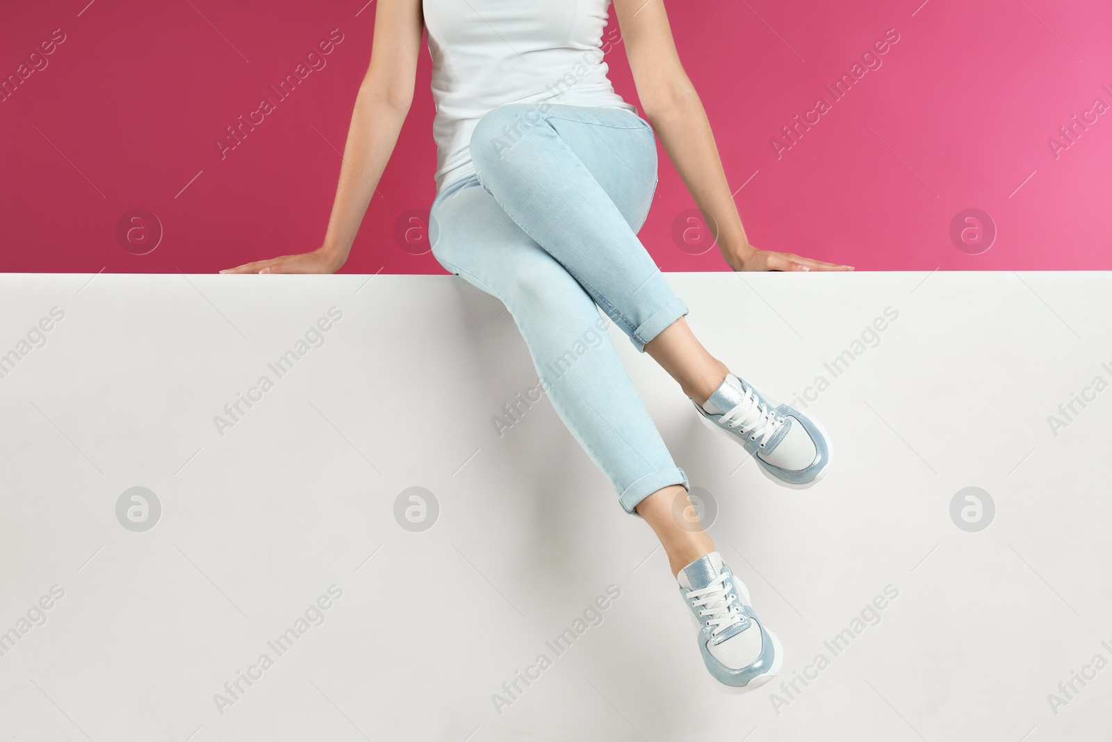 Photo of Woman in stylish sneakers sitting on color background, closeup