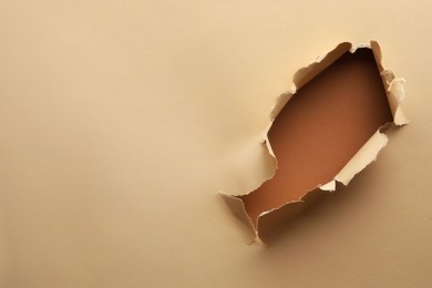 Photo of Hole in light beige paper on brown background, space for text