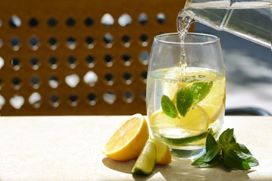 Photo of Woman pouring water into glass with lemon slices and mint at table, closeup. Space for text