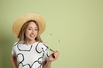 Photo of Beautiful young woman with straw hat and sunglasses on light green background, space for text. Stylish headdress