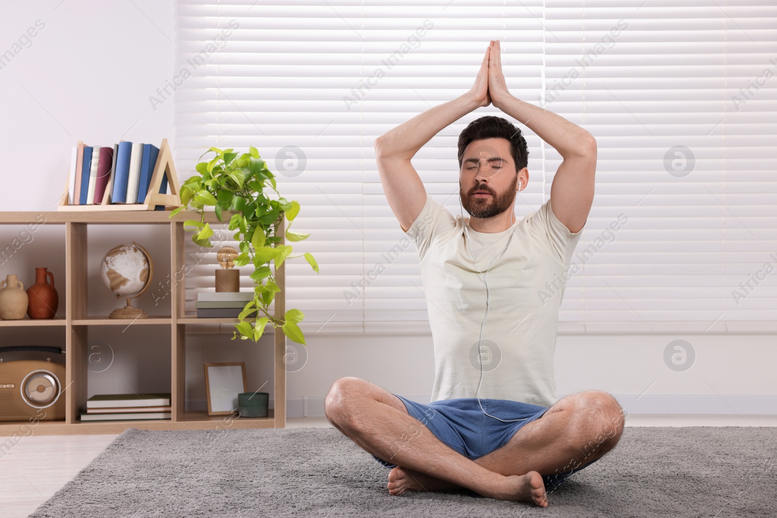 Photo of Man in earphones meditating at home, space for text