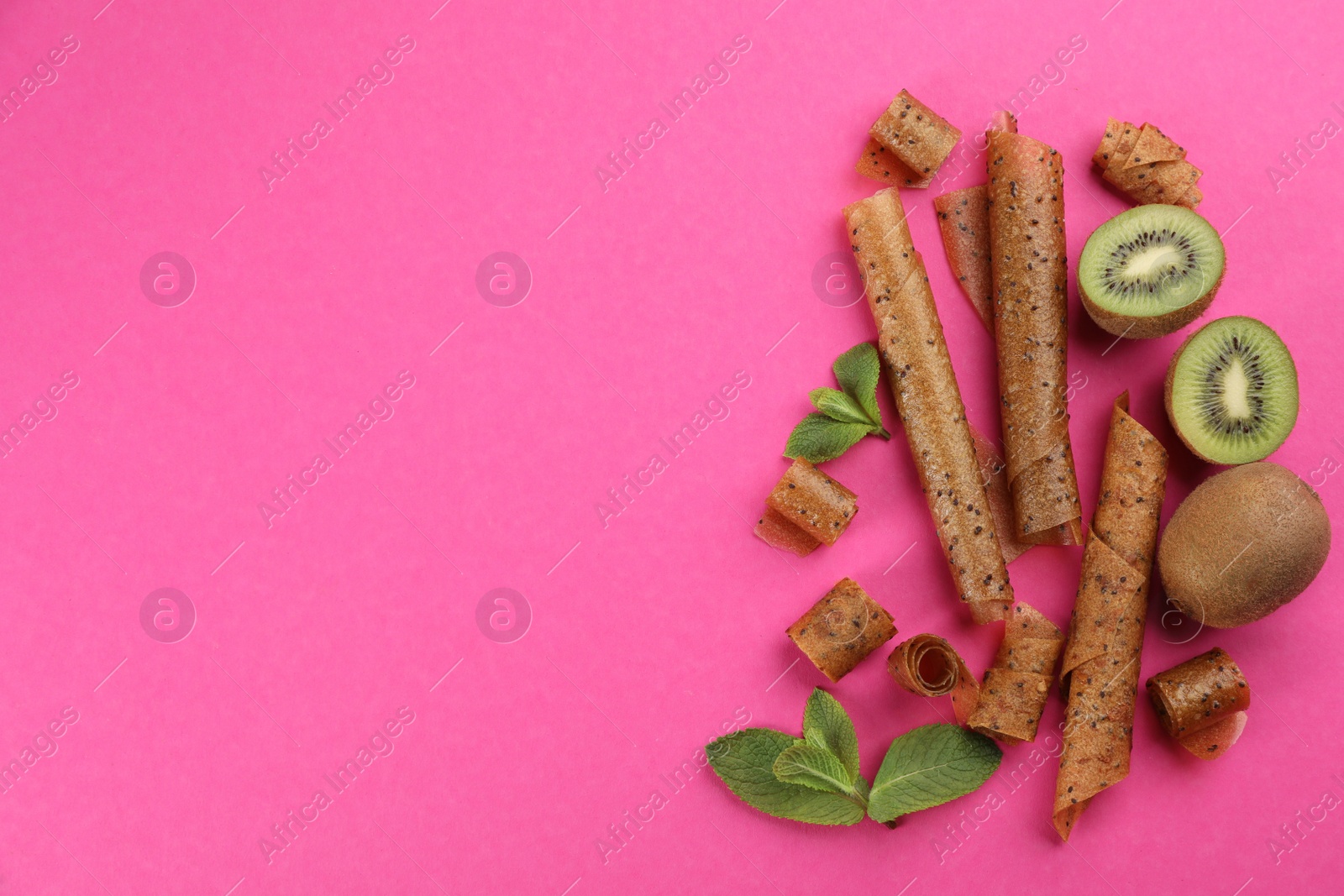 Photo of Delicious fruit leather rolls, mint and kiwis on pink background, flat lay. Space for text