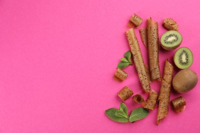 Delicious fruit leather rolls, mint and kiwis on pink background, flat lay. Space for text