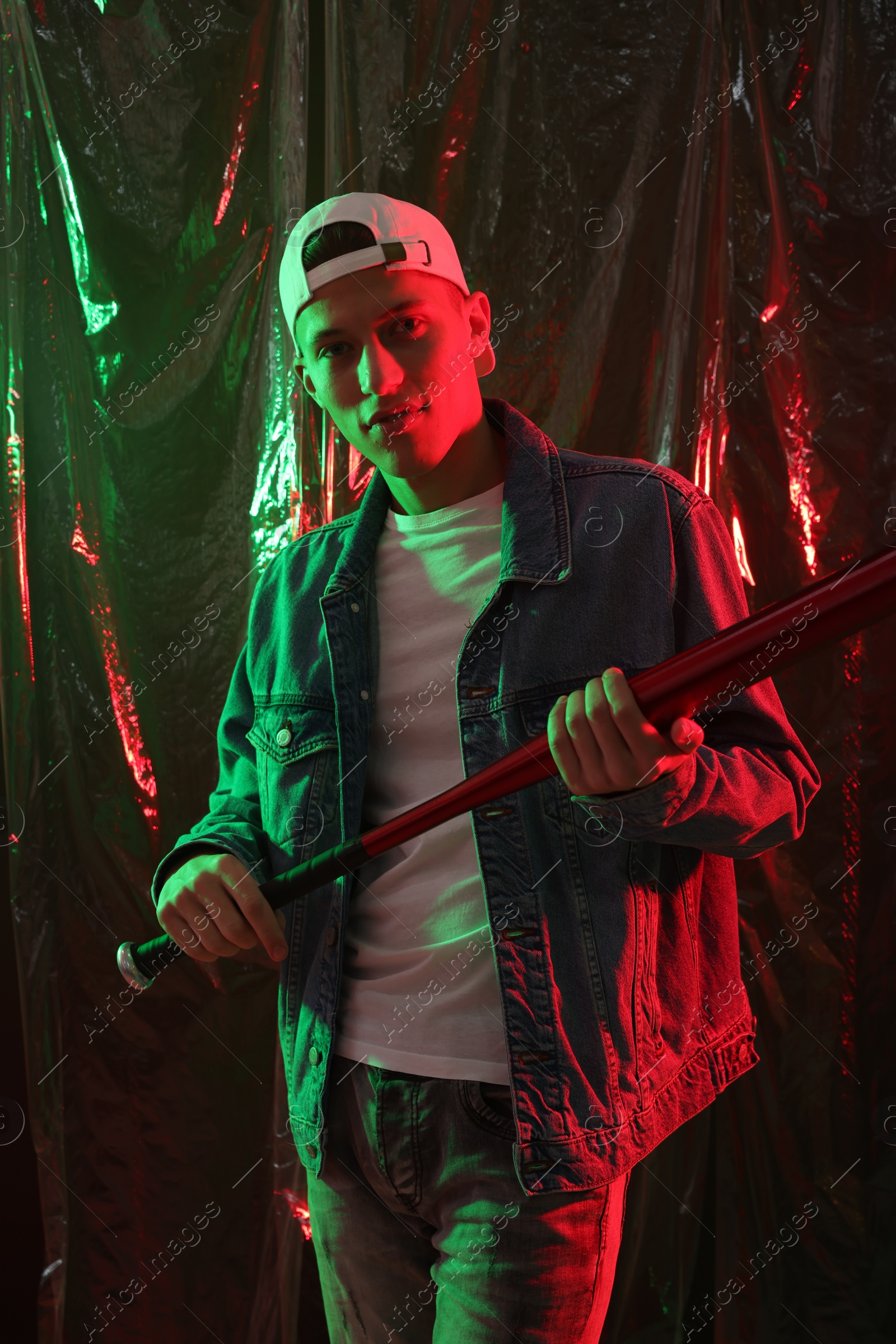 Photo of Young man with baseball bat on dark background in neon lights