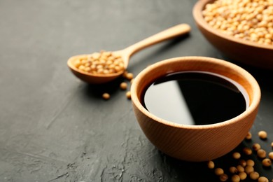 Photo of Tasty soy sauce in bowl and soybeans on black table, closeup. Space for text