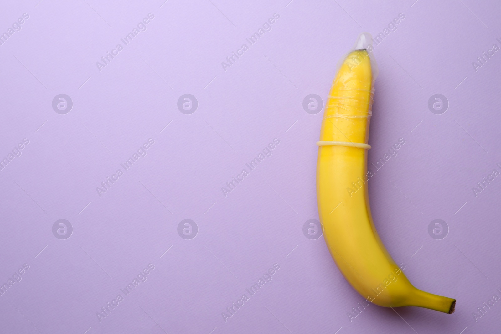 Photo of Banana with condom on lilac background, top view and space for text. Safe sex concept