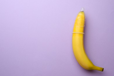 Banana with condom on lilac background, top view and space for text. Safe sex concept