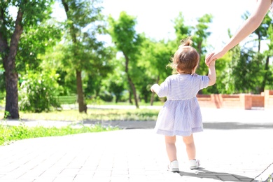 Photo of Adorable baby girl holding mother's hand while learning to walk outdoors